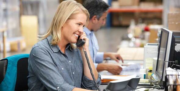 A woman sitting in an office talking on the desk phone while looking at her computer screen