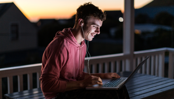 Young man on laptop with earphones, outside in the early morning.