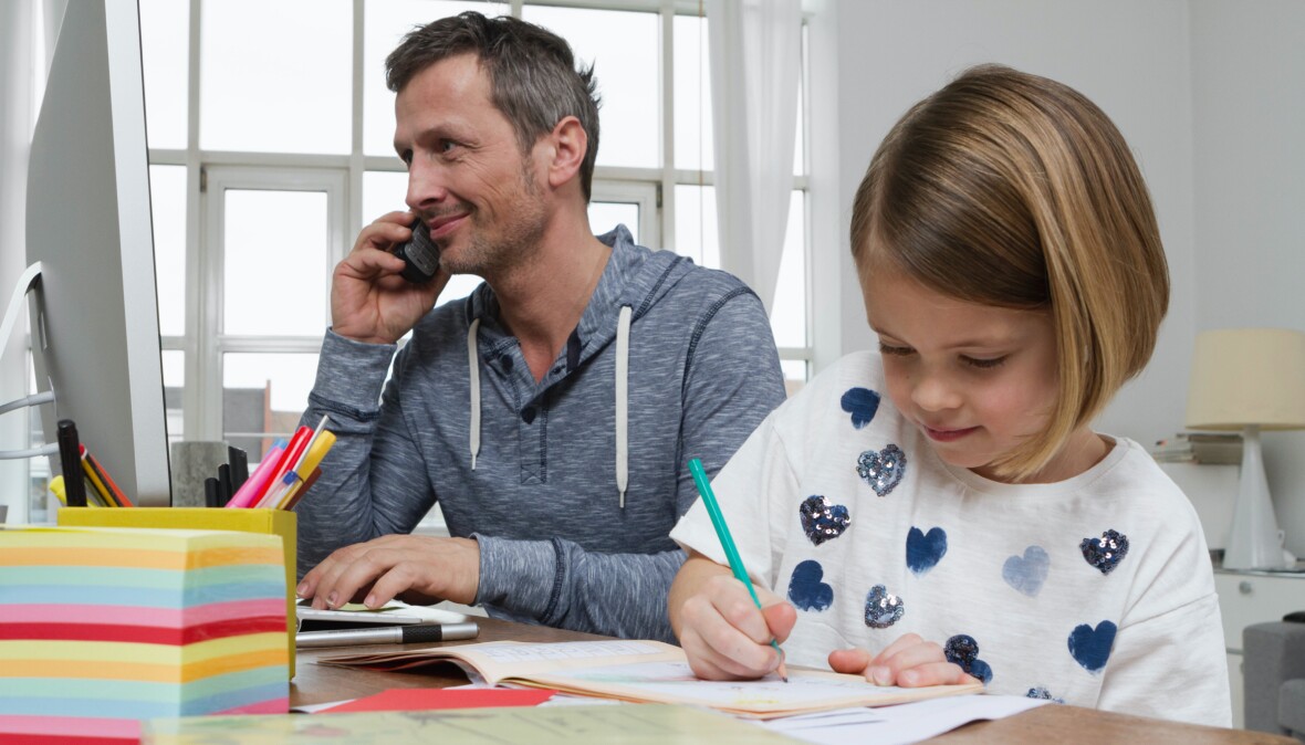 Man talking on the phone and his daughter writing in a notebook.