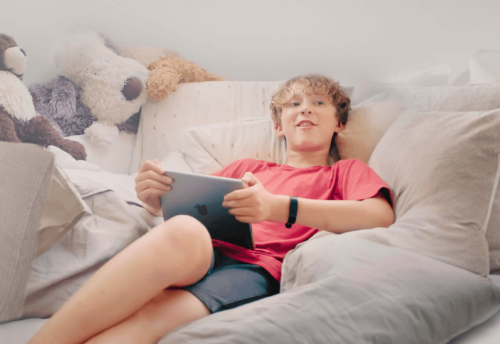 Boy sitting on his bed holding an iPad and smiling