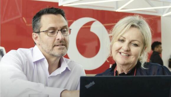 A man and woman talking in front of a laptop at a Vodafone Store
