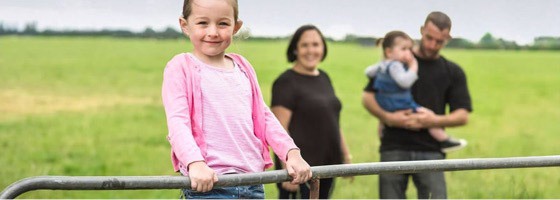 A family standing together by a gate on a farm