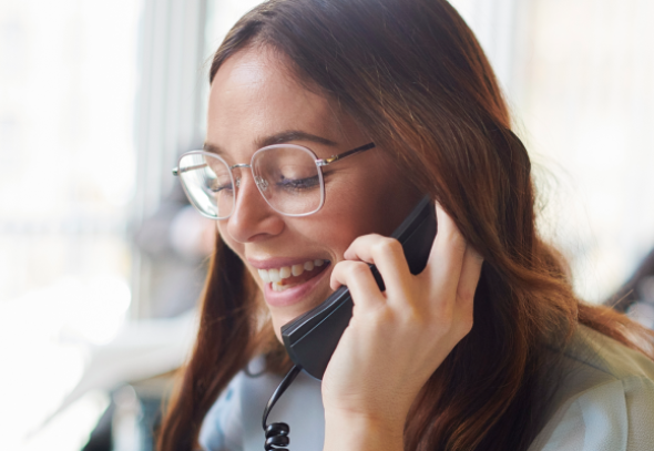 Female wearing glasses and long hair holding a landline phone