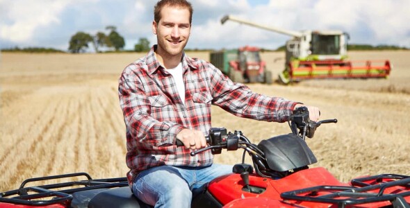 Maize farm worker on quad bike in front of combine harvester loading