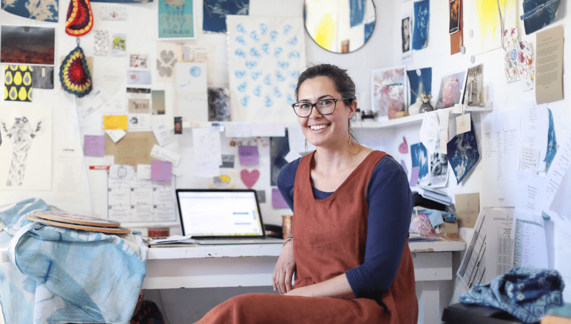 A woman in a room smiling with laptop on table