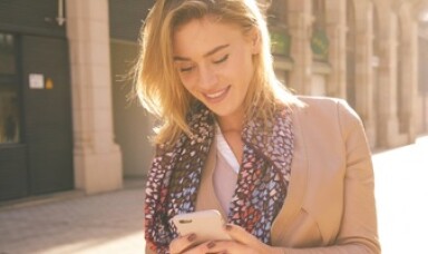 A woman outdoors walking down the street looking at her phone