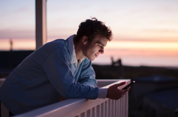 A man, in twilight, checking details on his phone. 