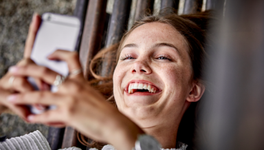 A carefree girl lying down, smiling at her phone screen.