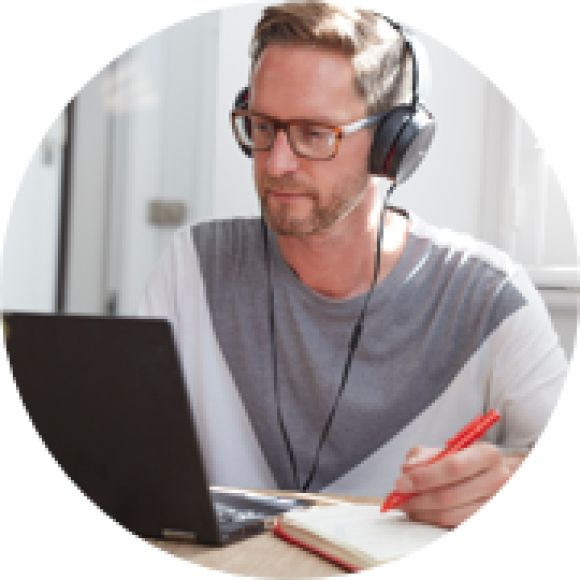 Image of person with headphones on writing in a notepad