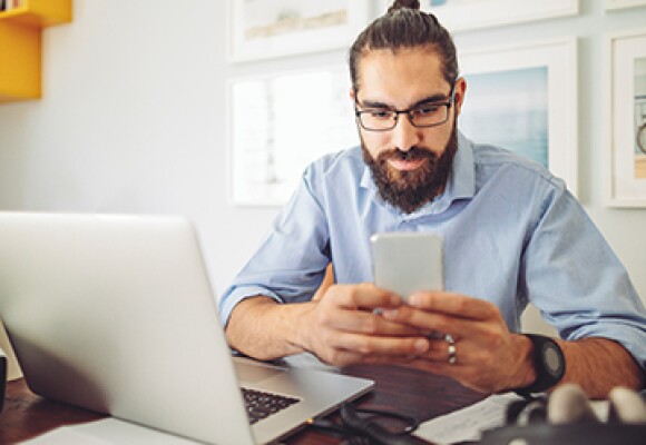 Man looking at a phone with a laptop next to him