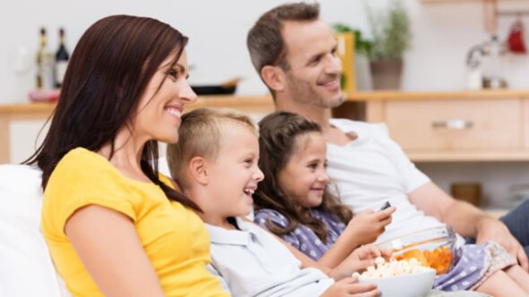 A family of four smiling and watching tv eating popcorn.