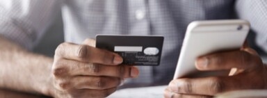 Person in checkered shirt holding a credit card and mobile phone