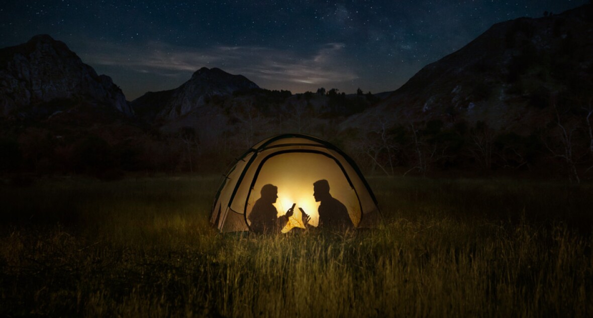 Two people using mobile phone in a tent at night