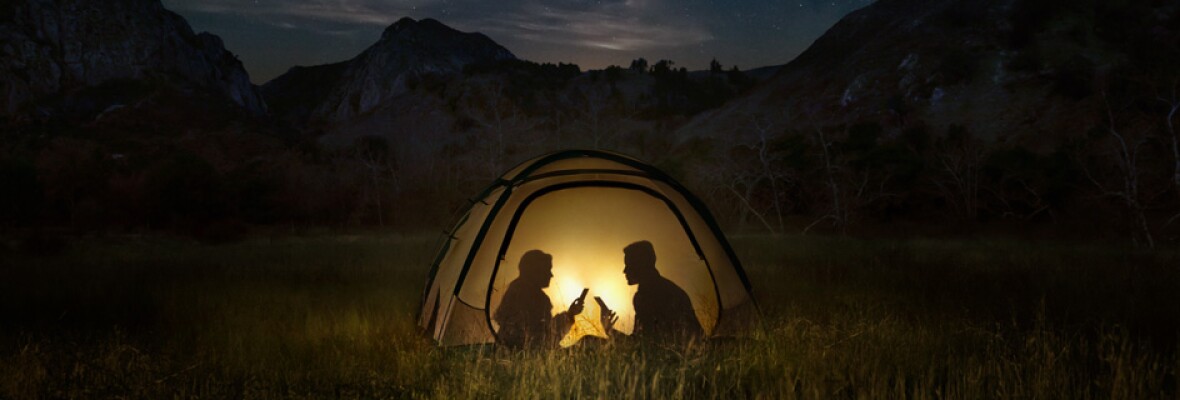 Two people using mobile phone in a tent at night