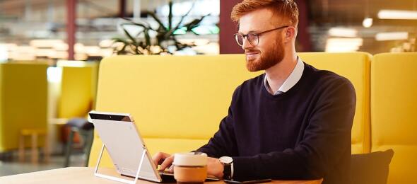 Guy working on laptop tablet with coffee in a shared office locale