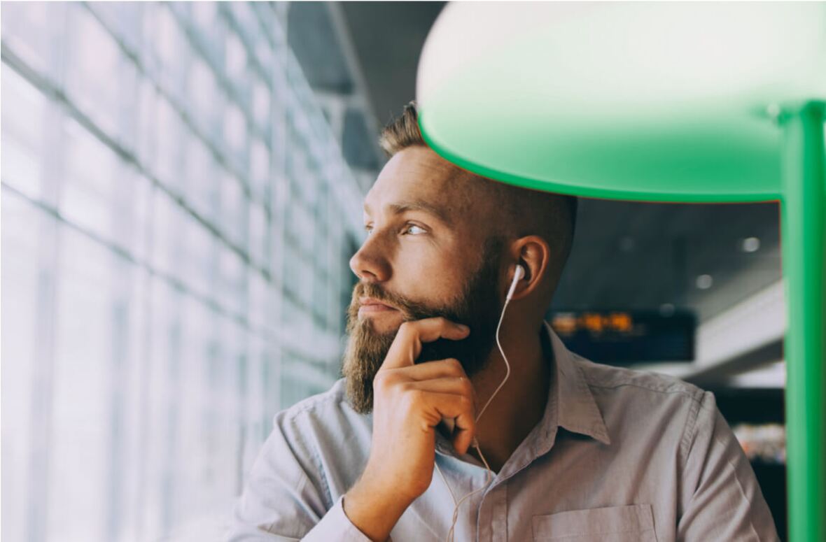 man with beard looking out the window in a collared shirt wearing earphones