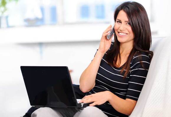 Woman in striped shirt talking on the phone and using a black laptop
