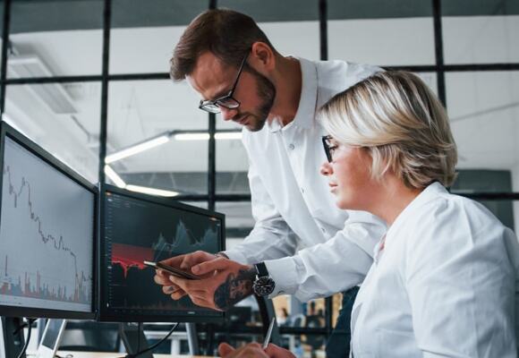 Two workers in a stock exchange looking at computer monitor showing stock trading