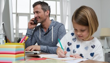 Man talking on the phone and his daughter writing in a notebook.