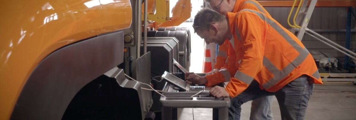 Two workers looking at laptops in a truck factory