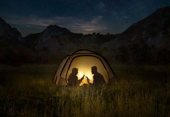 Two people using mobile phone in a tent at night