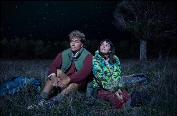 Jade and pippa sitting on grass looking towards sky.
