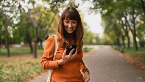 A lady walking through a city park, glancing at her phone.