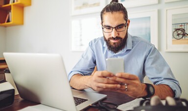 Man looking at a phone with a laptop next to him