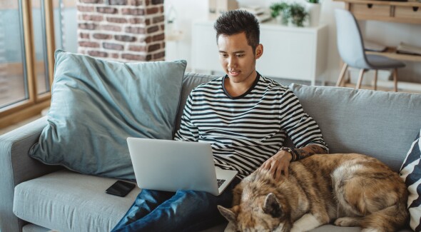 Man web-browsing with his laptop, beside a dog.