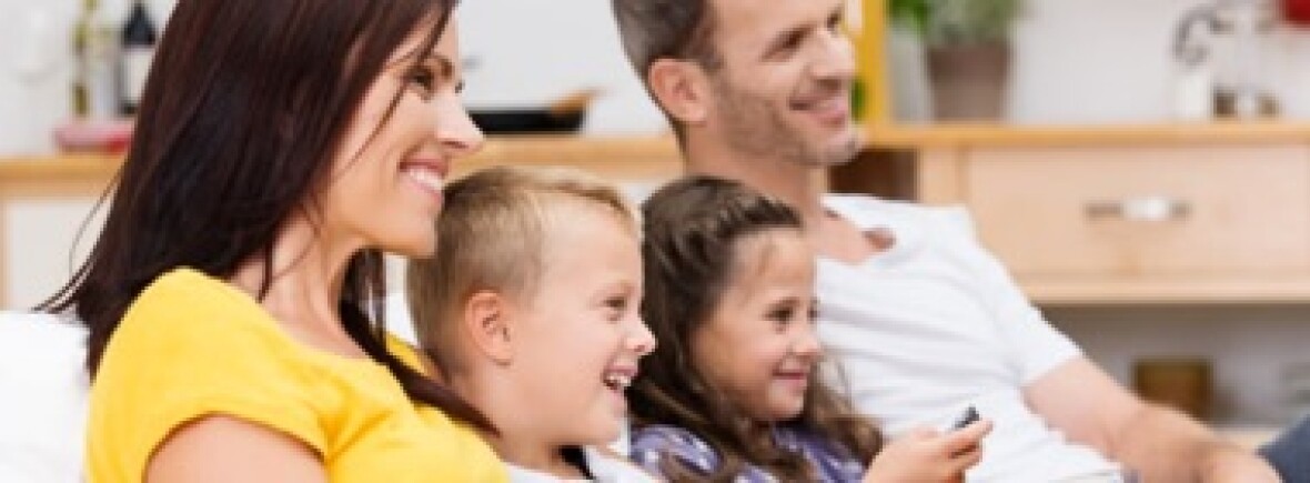 Family of 4 sitting on a chair together watching VodafoneTV