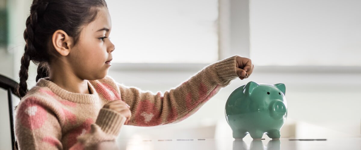 A young girl dropping a coin in to a Piggybank.