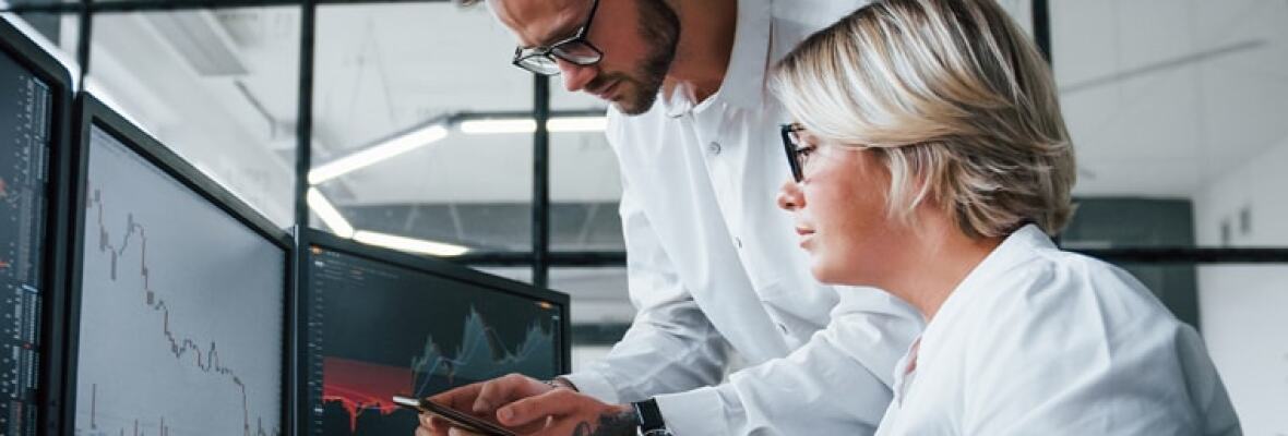 Two workers in a stock exchange looking at computer monitor showing stock trading