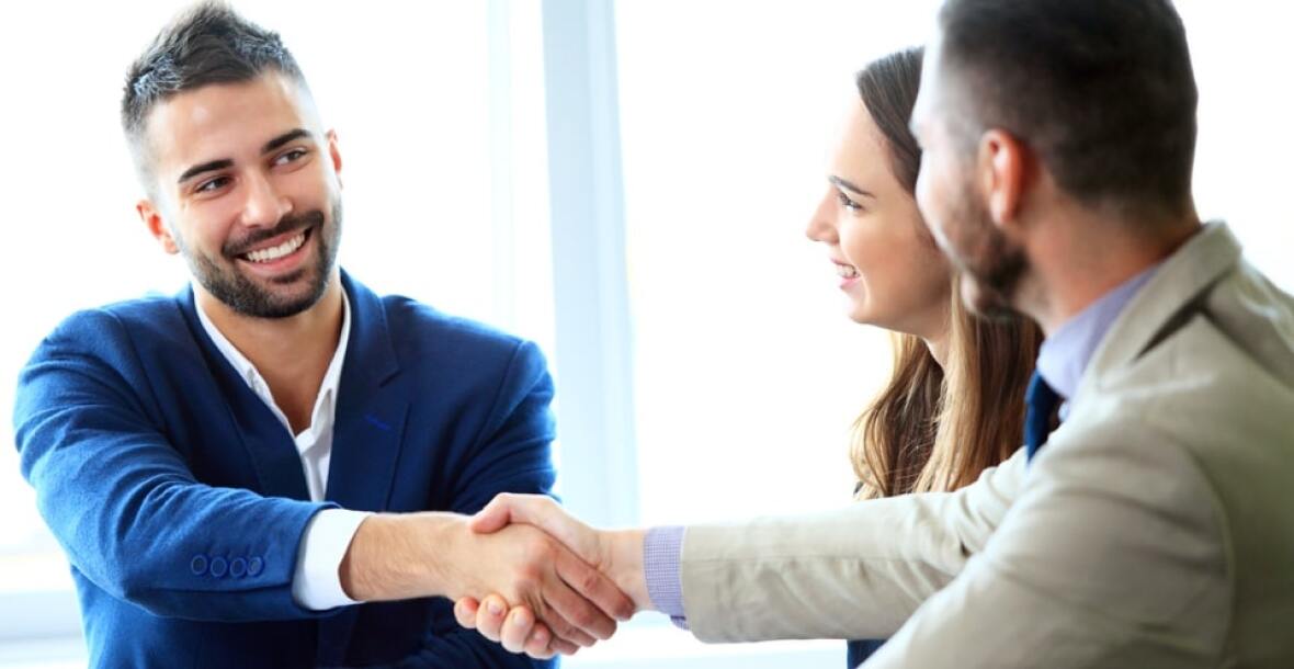 Two men shaking hands and a woman looking at them