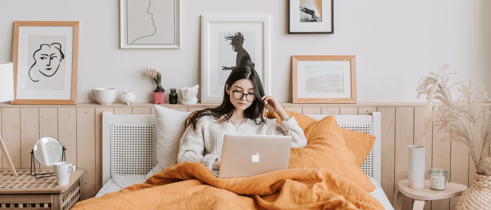 A woman, relaxed on her bed, using a MacBook laptop.