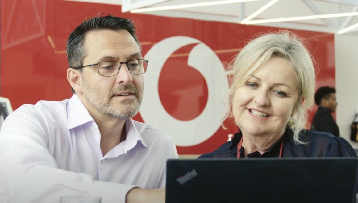 A man and woman talking in front of a laptop at a Vodafone Store