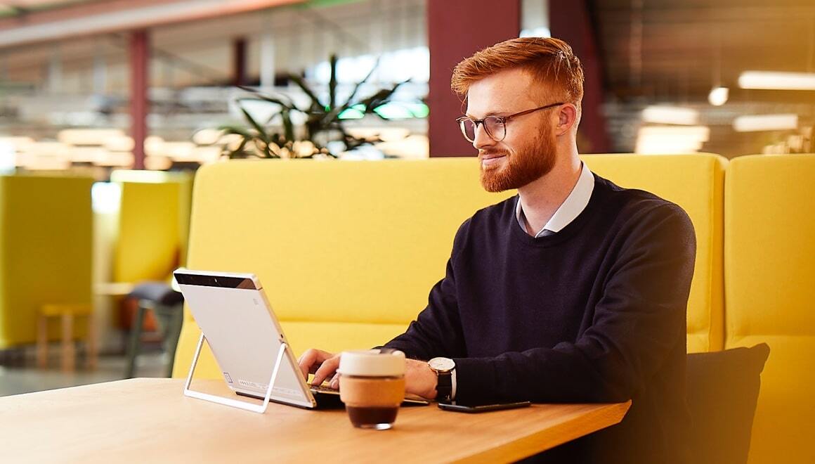 Guy working on laptop tablet with coffee in a shared office locale