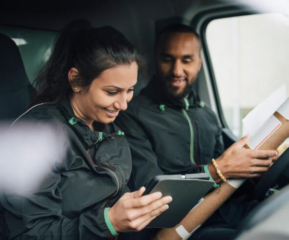 Two delivery drivers in a van checking delivery orders