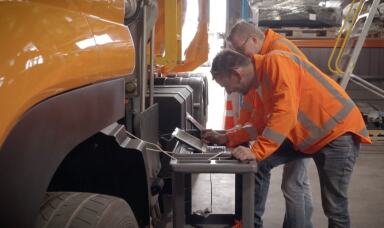 Two workers looking at laptops in a truck factory
