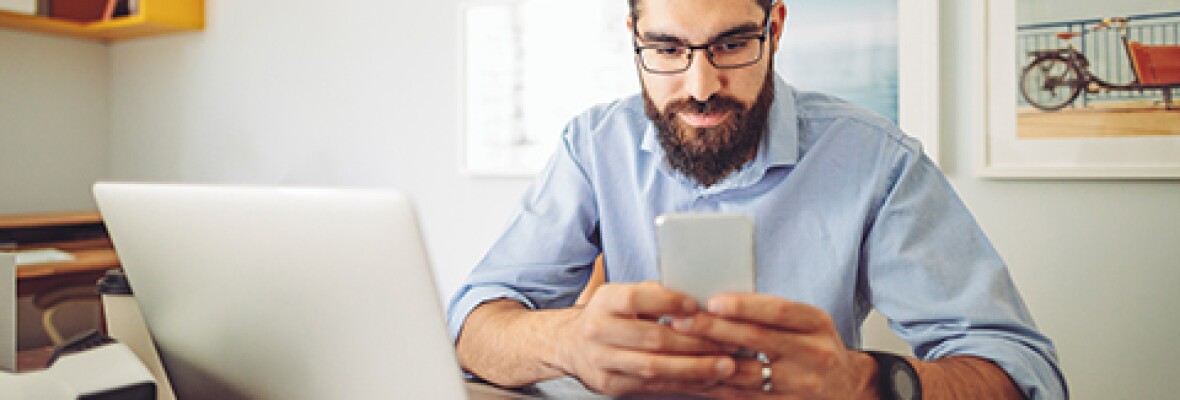 Man looking at a phone with a laptop next to him