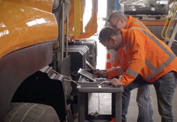 Two workers looking at laptops in a truck factory