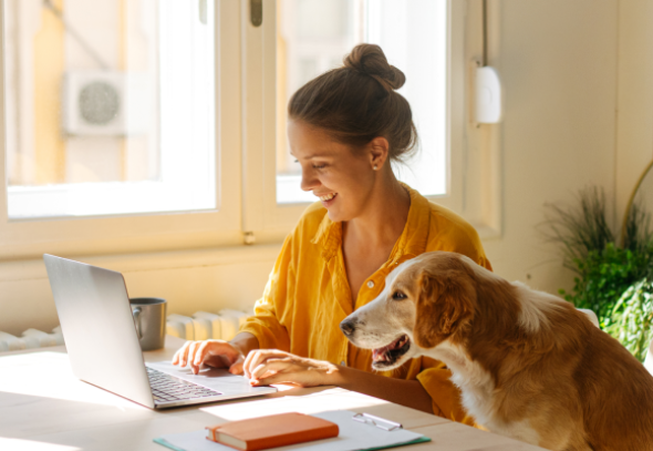 Woman wearing yellow on a laptop with a dog beside her