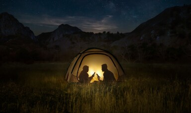 Two people using mobile phone in a tent at night