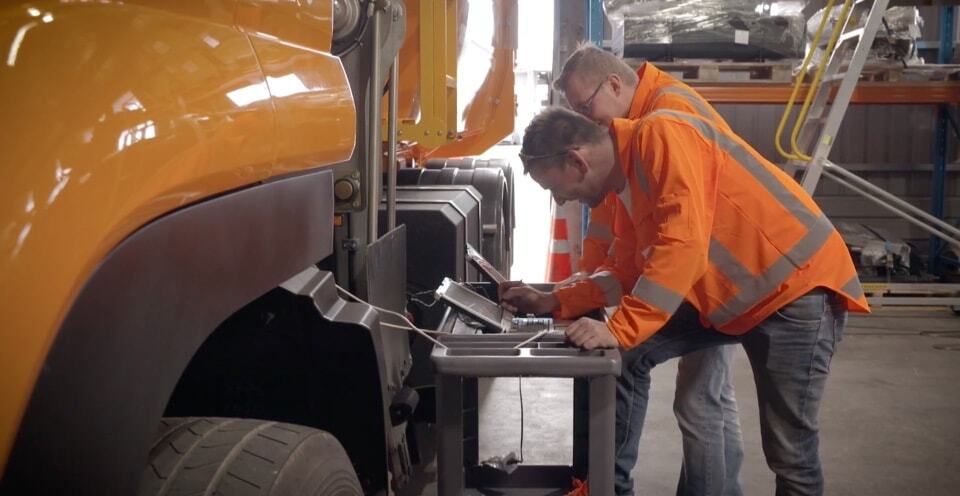 Two workers looking at laptops in a truck factory