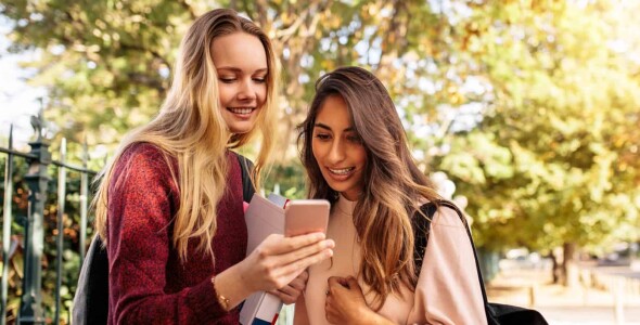 2 female university students checking out class schedules on device