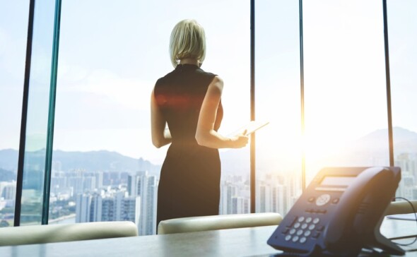 Woman looking out of a window of a big building with SIP phone on a table