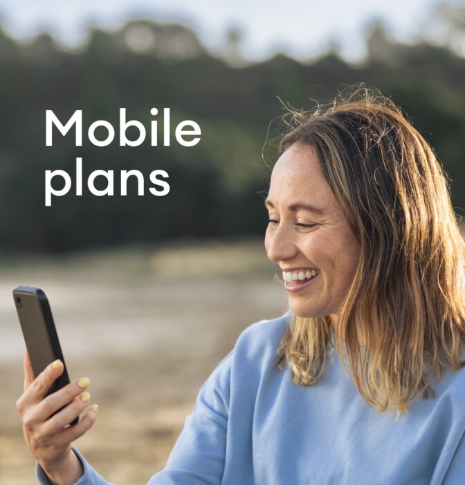 A lady smiling at what's showing on her mobile phone, as she sits on a quiet beach.
