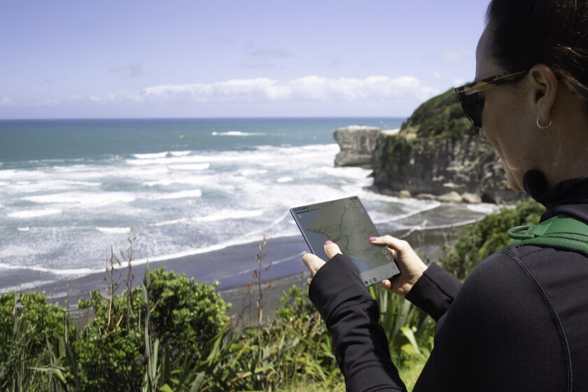 A lady using her phone at a remote beach location with One NZ.