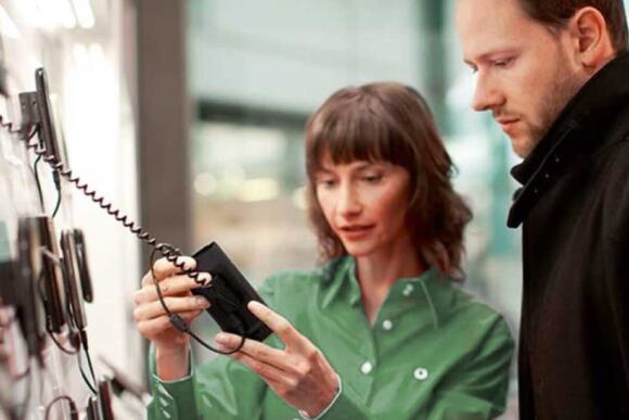 woman in green shirt showing man in black shirt a phone device attached to the wall