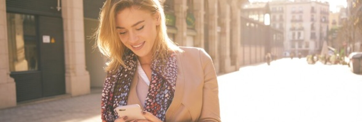 A woman outdoors walking down the street looking at her phone