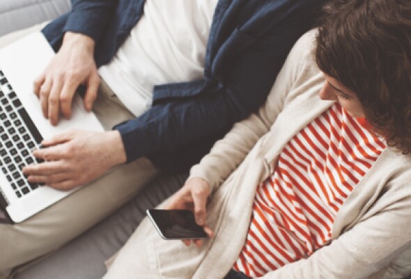 A woman and a man sitting on the couch using technology.
